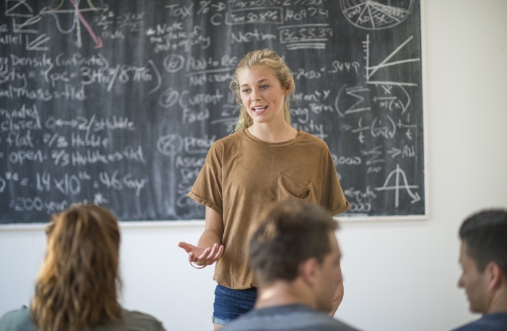 Woman in front of black board teaching 